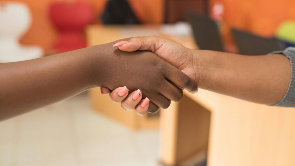 Two women exchanging a handshake in a professional indoor office setting.